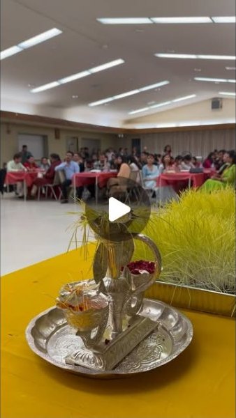 A hall filled with people seated at decorated tables, with a puja thali in the foreground.